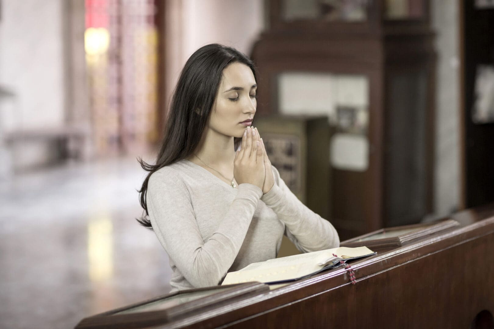 A woman praying inside a church, eyes closed in meditation.