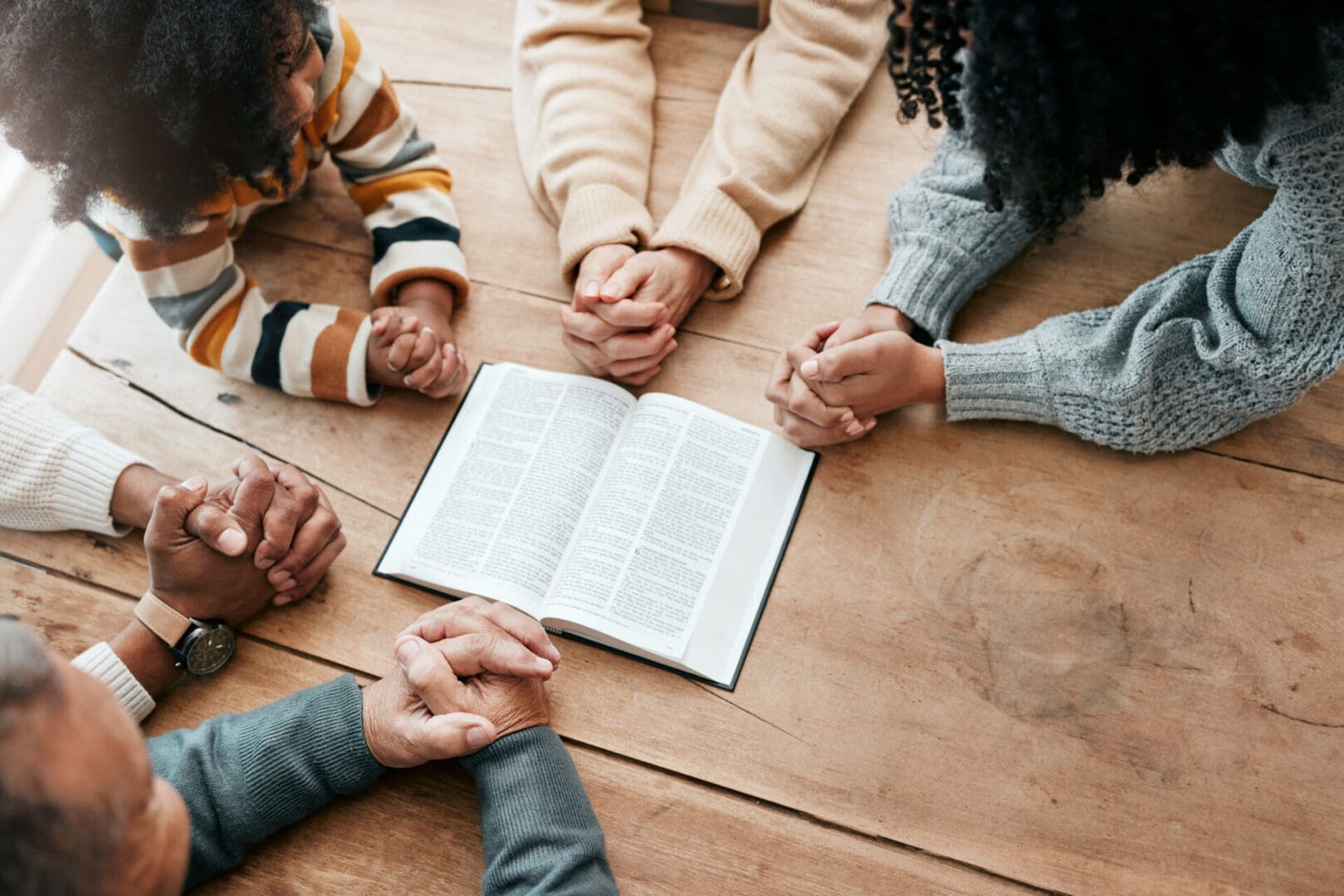 Group holding hands around an open book, symbolizing unity and faith.