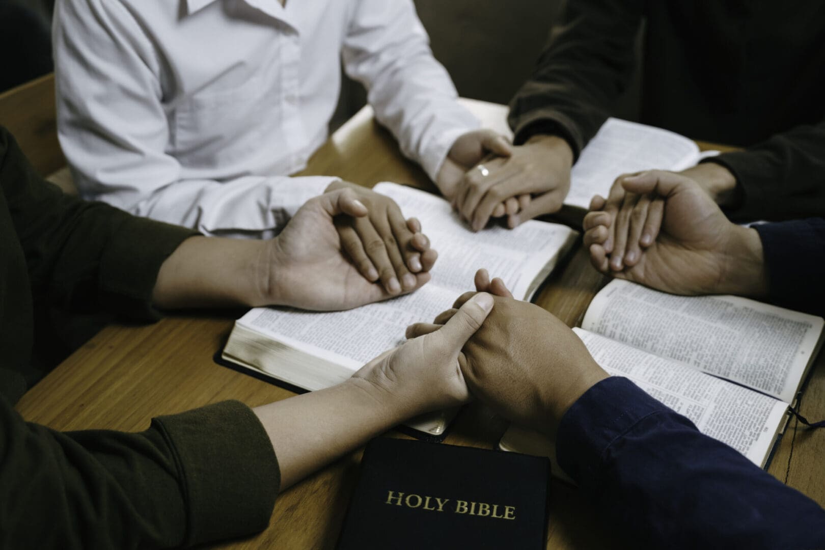 A group holding hands in prayer around an open Bible.
