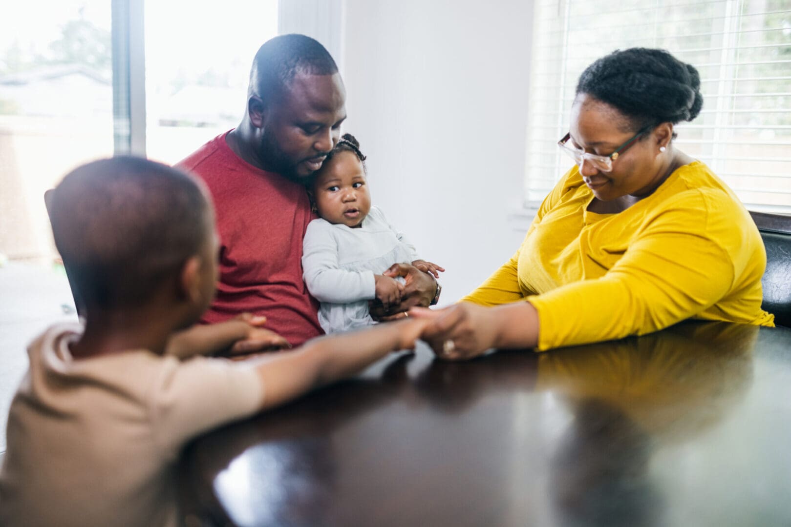 Family holding hands in prayer around a table.