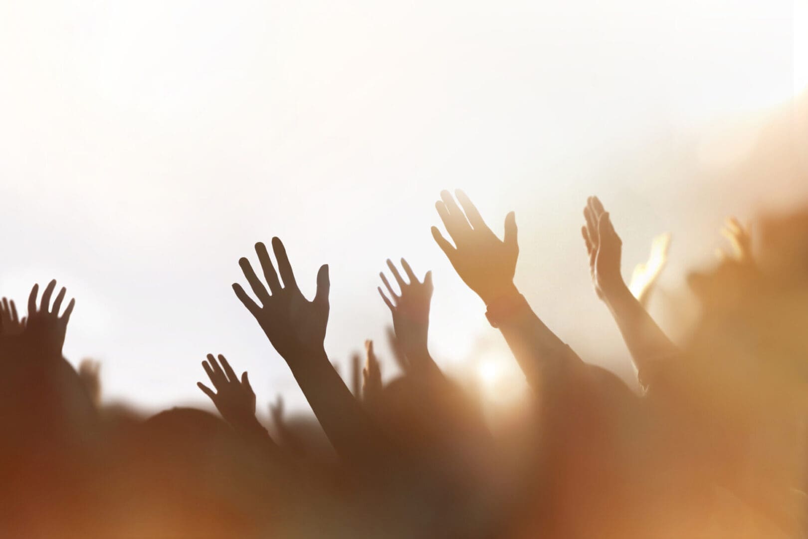 Hands raised in celebration or worship against a bright sky.