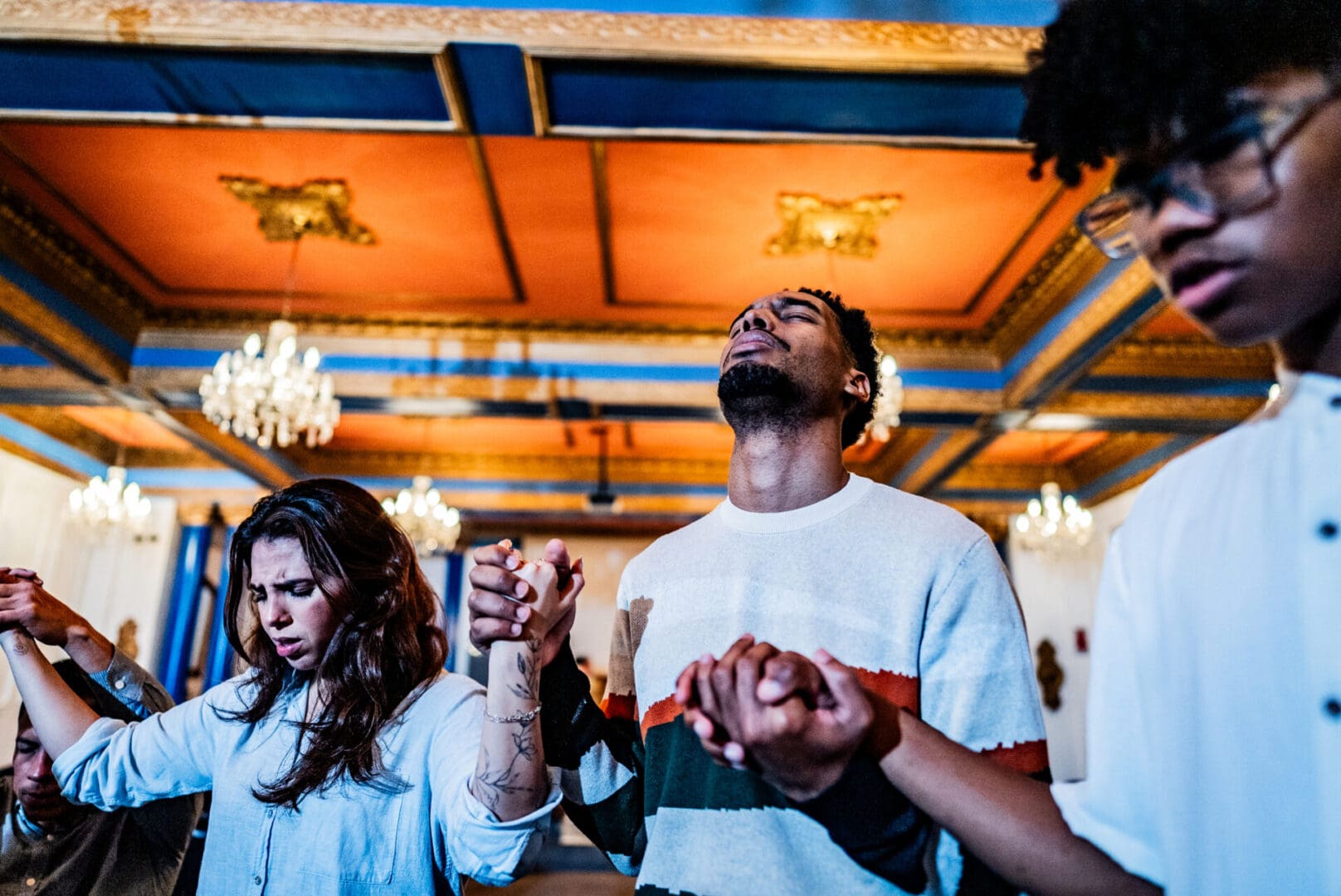 People holding hands in prayer in a vibrant room.
