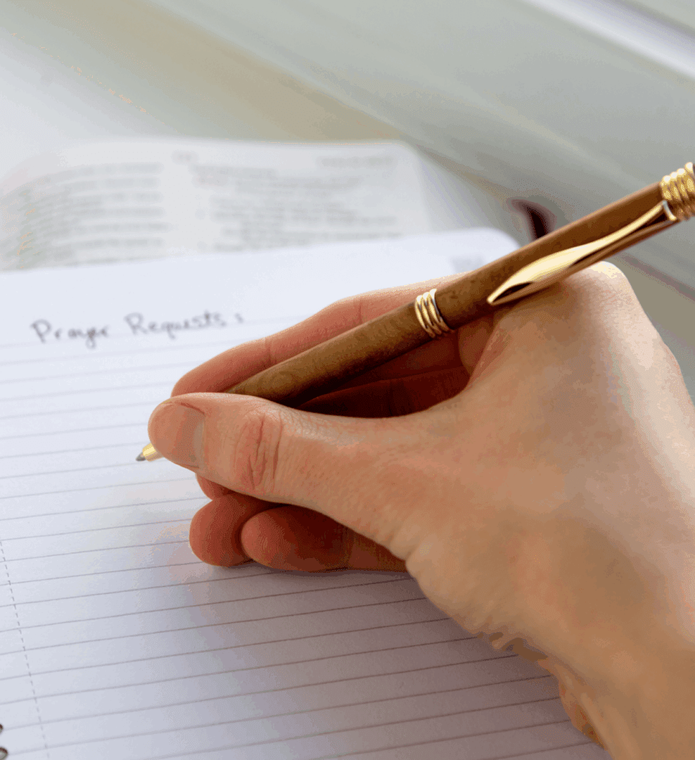 A person writing 'Page One' on a lined notebook with a pen.