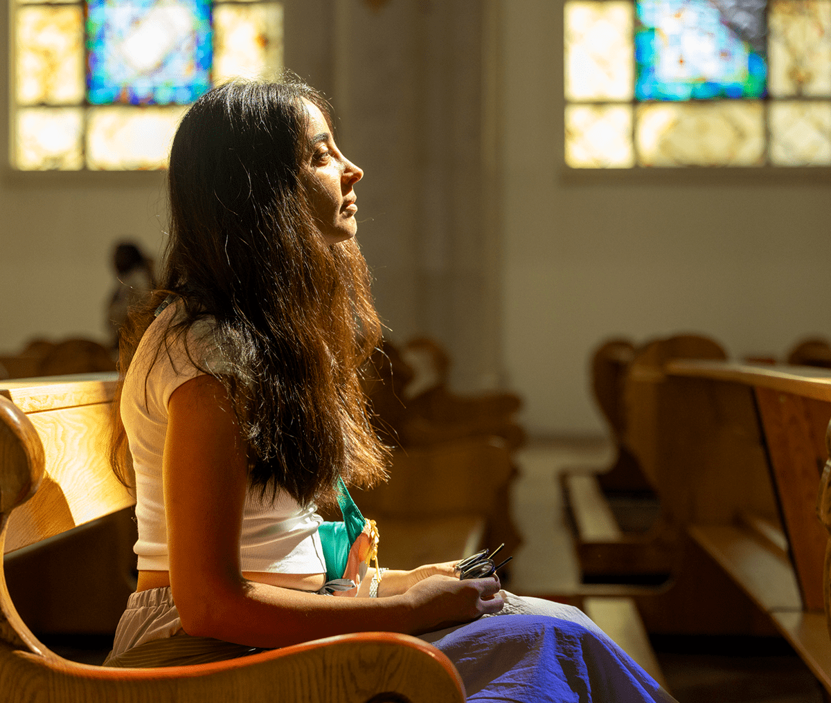 A woman sitting in a church pew, bathed in sunlight.