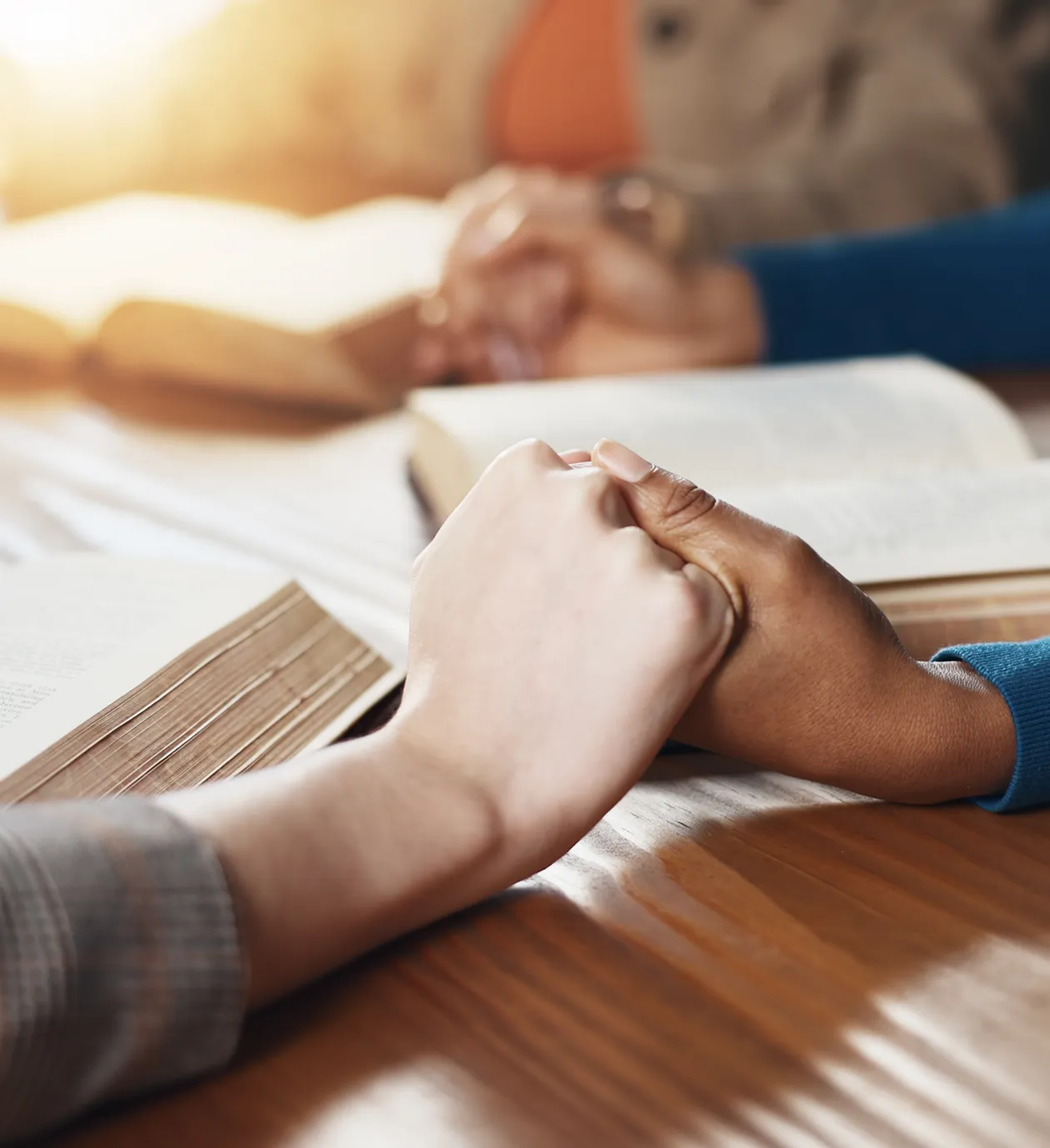 Two people holding hands over an open book in a warm setting.