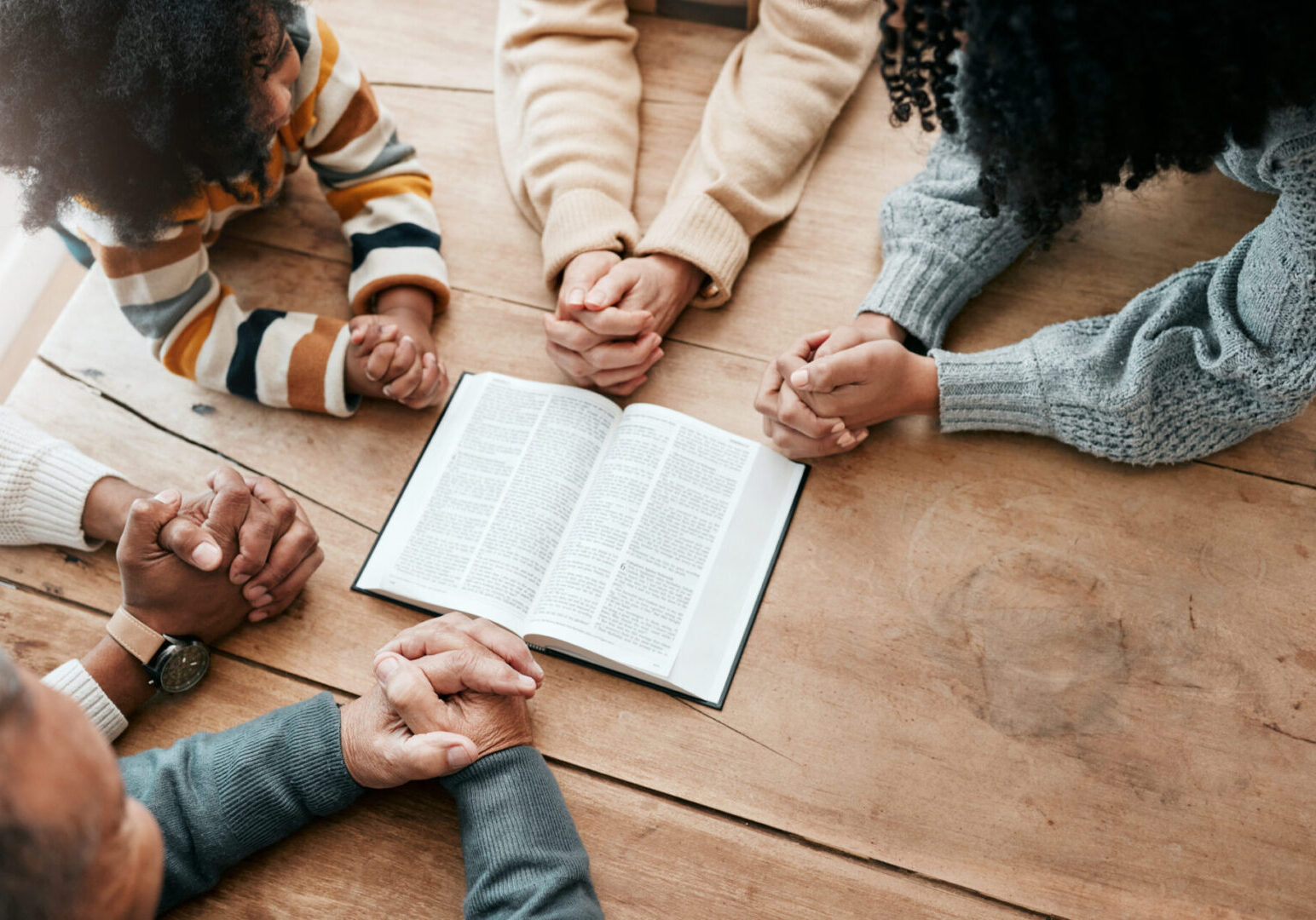 Group holding hands around an open book, symbolizing unity and faith.