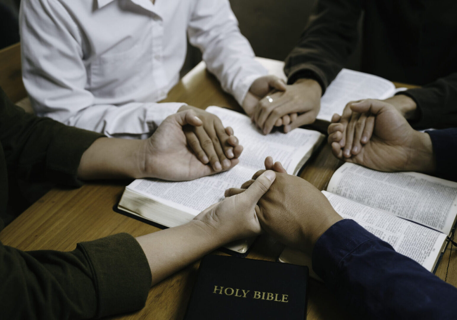 A group holding hands in prayer around an open Bible.
