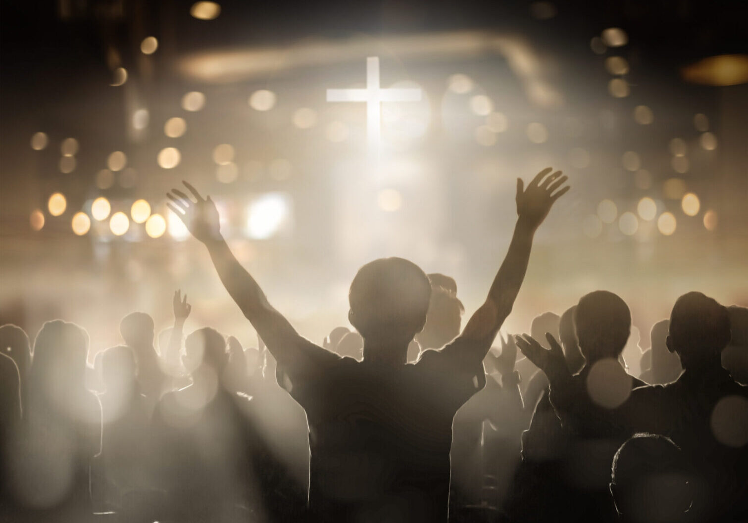 Person raising hands in worship for a glowing cross