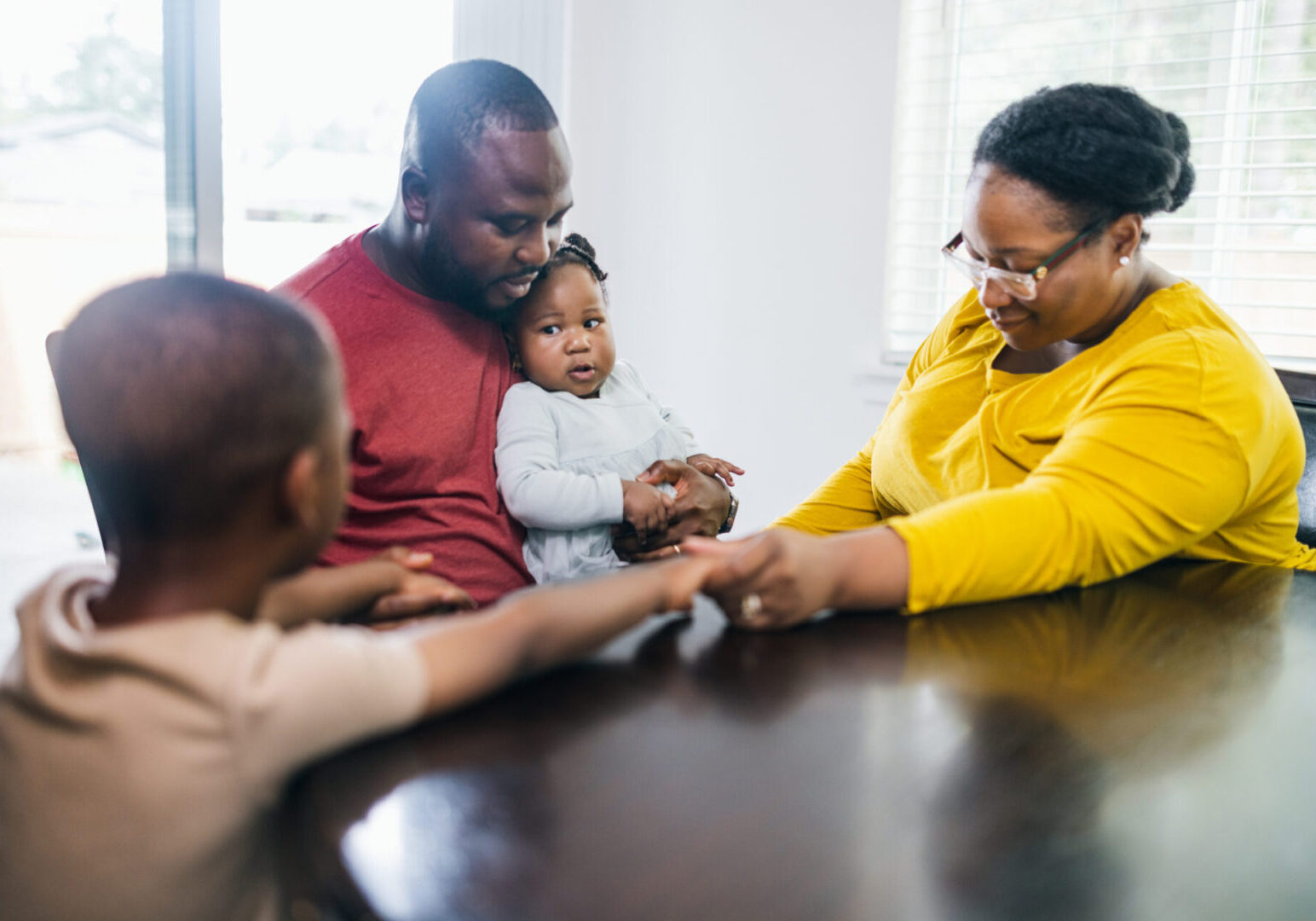 Family holding hands in prayer around a table.