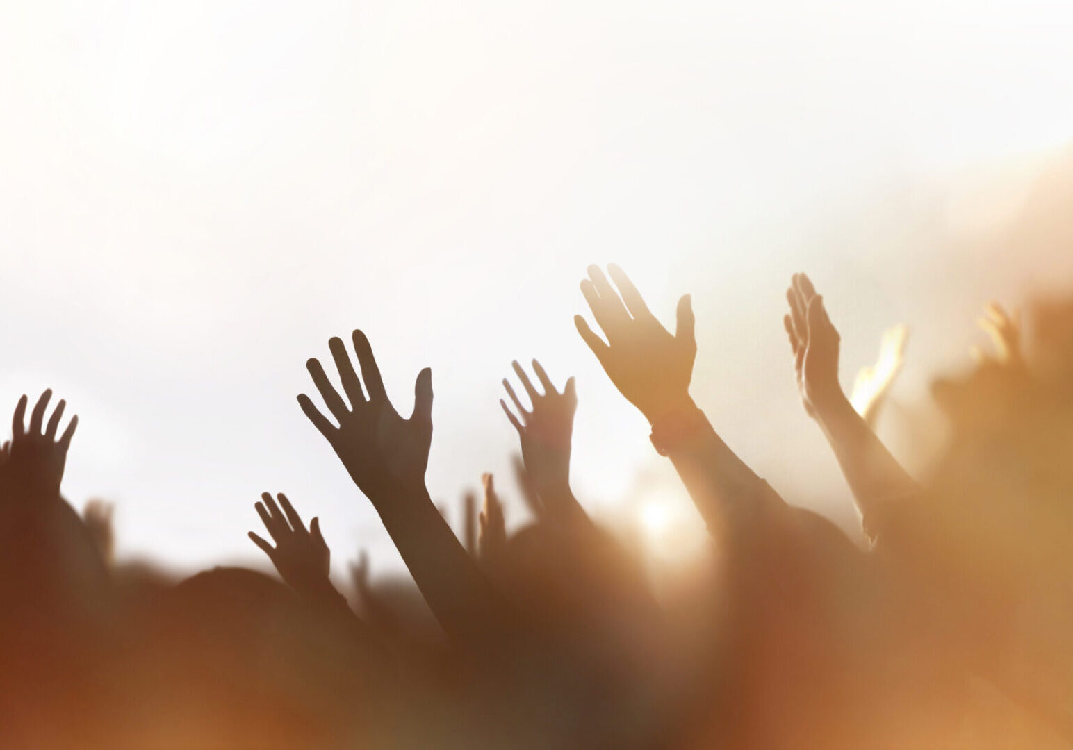 Hands raised in celebration or worship against a bright sky.